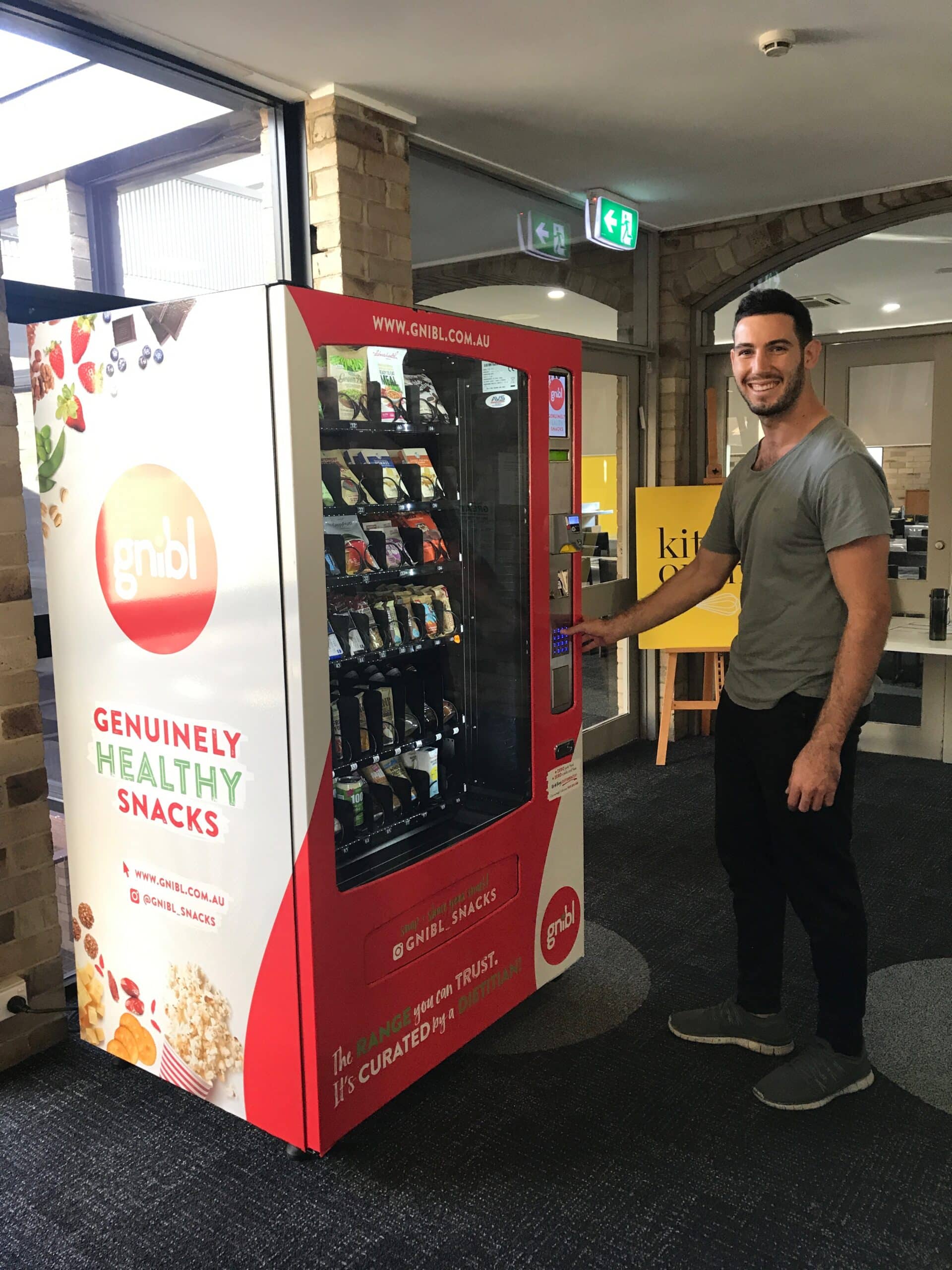 A smiling patron interacting with a Gnibl vending machine at a workplace.
