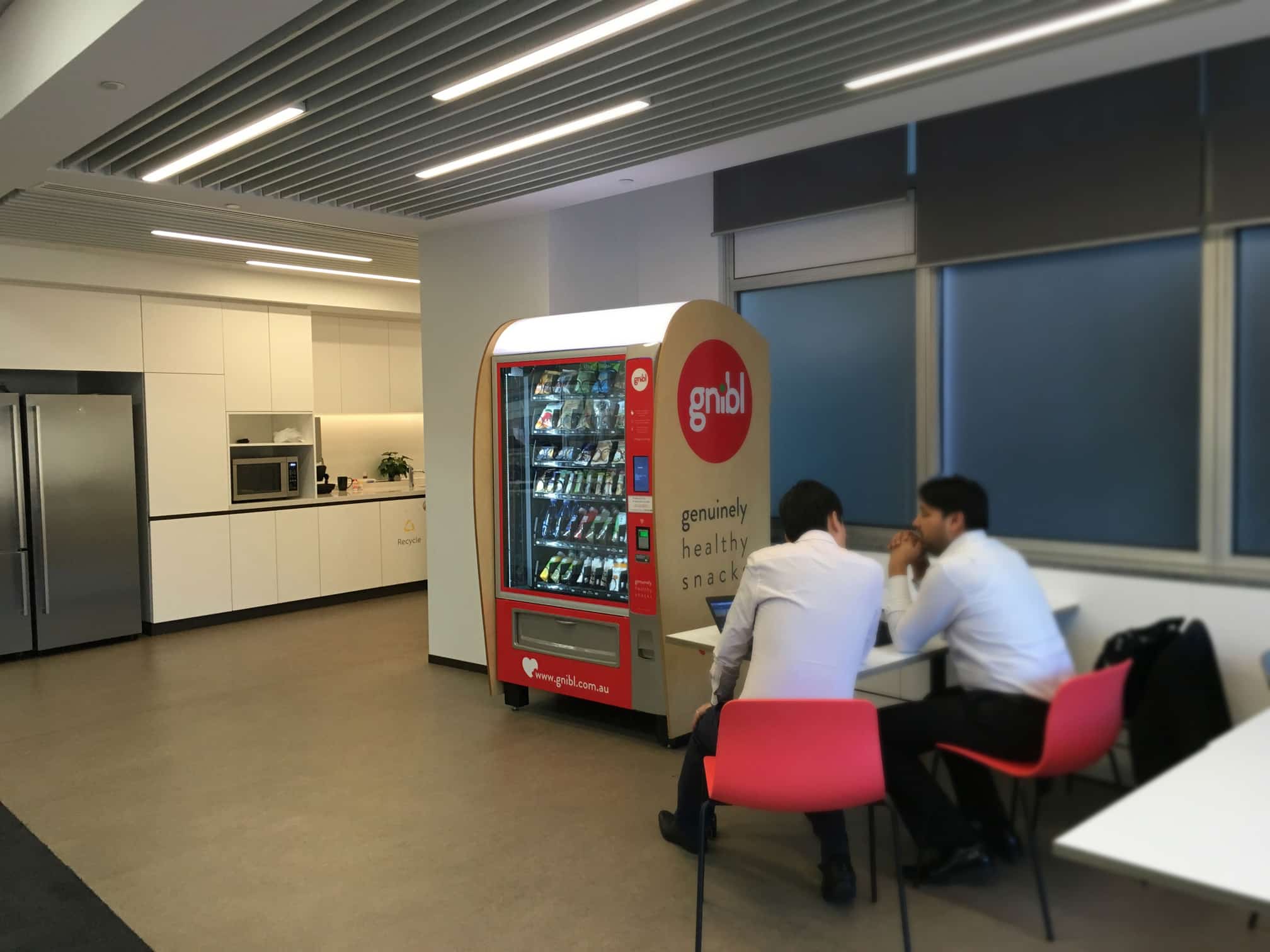 Gnibl Vending machine placed in an office workplace with two workers talking in the foreground.