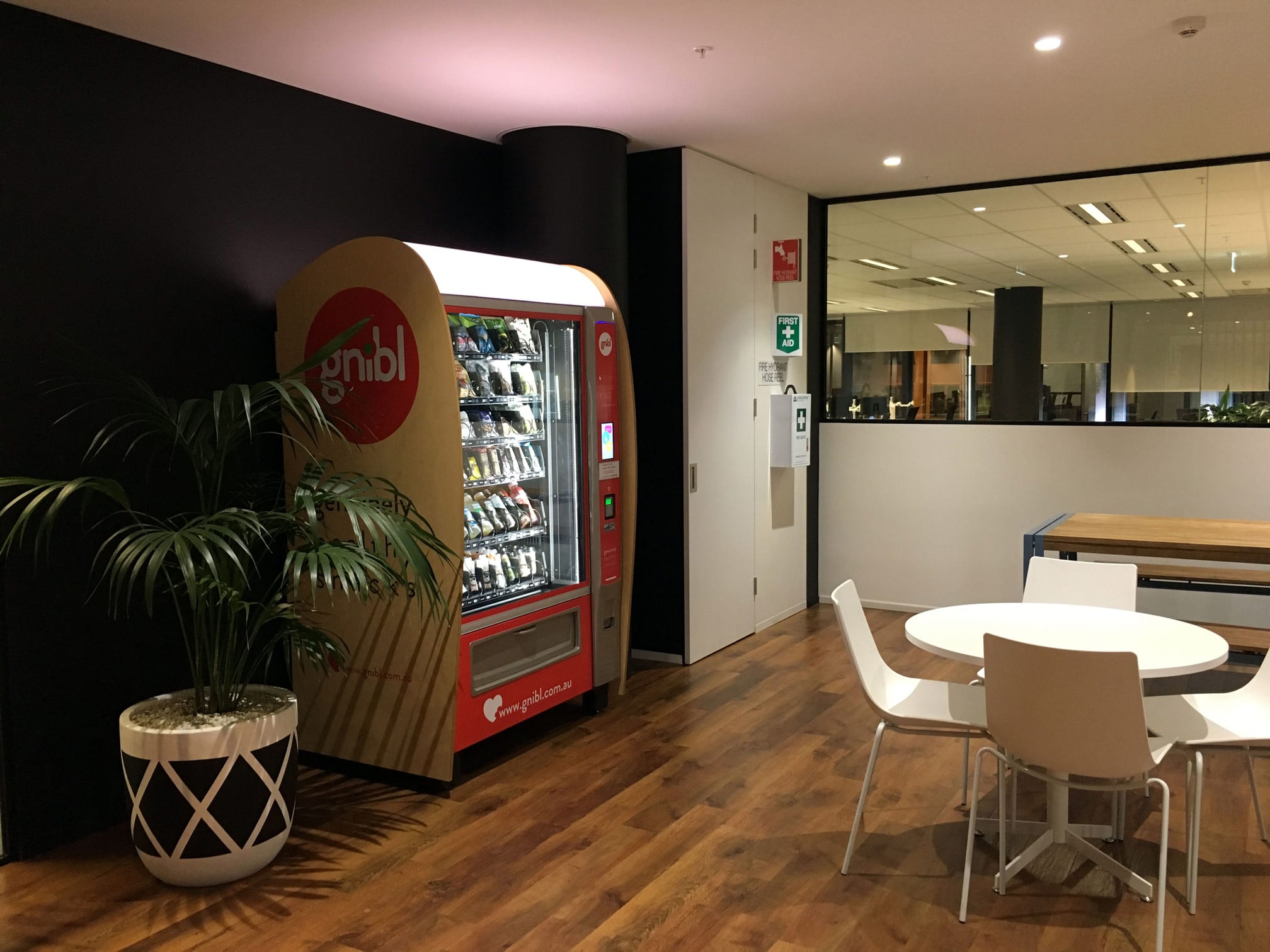 Gnibl Vending machine placed in an office environment with indoor plants, tables, and seating.