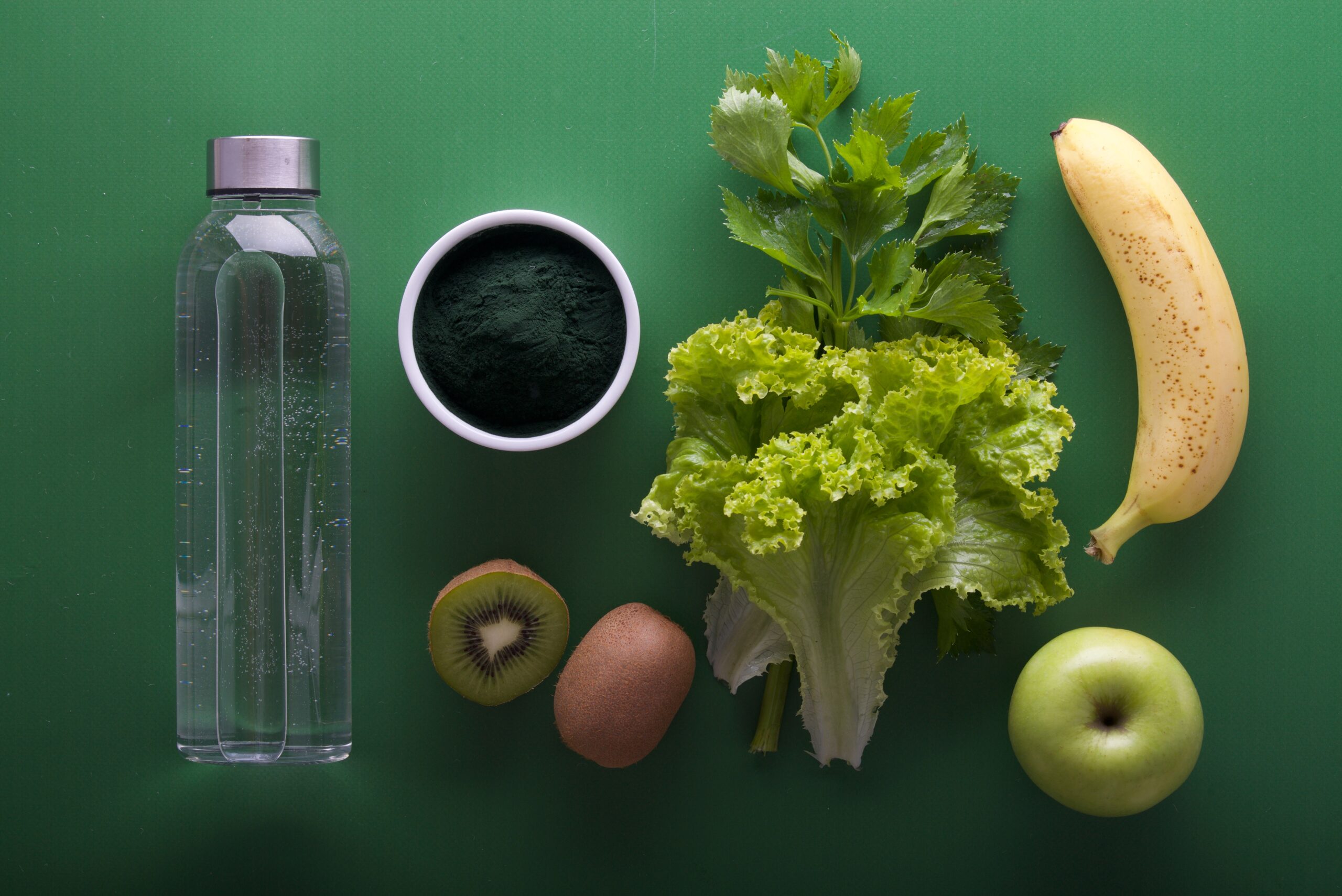 green and yellow fruit and vegetables and a bottle of water on a green background